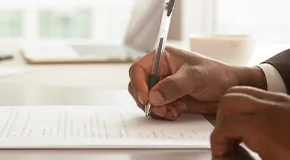 Person holding pen towards a contract lying on a table