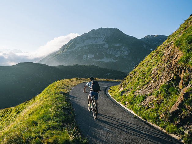 Person riding a bike uphill on a road in the mountains